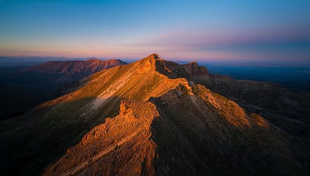 Golden sunrise on jagged mountain ridge with long shadows and alpine summit panorama vista