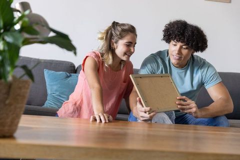 Young couple unpacking picture frame in cozy minimalist living room