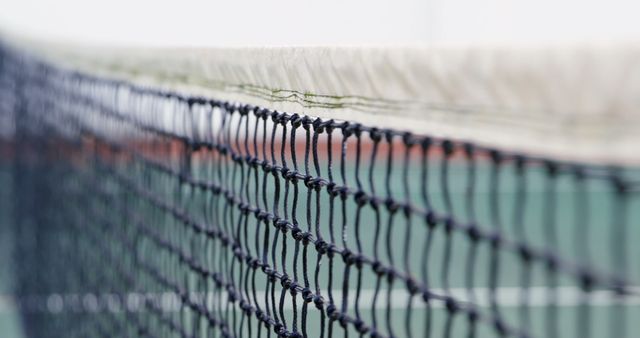 Detailed view of tennis net on outdoor court. Ideal for sport-related materials, equipment-focused campaigns, or fitness lifestyle promotions. Useful for illustrating articles, blog posts, or social media content about tennis, outdoor activities, or sports gear.