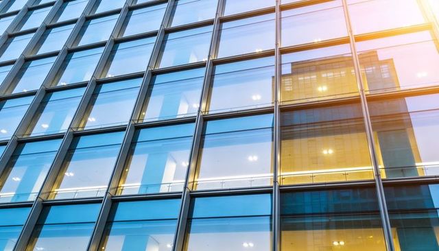 Reflecting glass facade creating geometric grid of city towers, blue sky and warm light