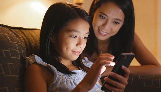 Mother and daughter connecting over smartphone sharing smiles cozy evening family bonding