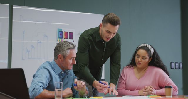 Image shows a diverse team collaborating in a business meeting, planning around a table with a whiteboard. Suitable for illustrating teamwork, corporate strategy discussions, and collaborative working environments.