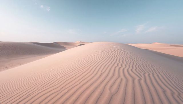 Expansive sand dunes showing rippled wind patterns under soft pastel sky