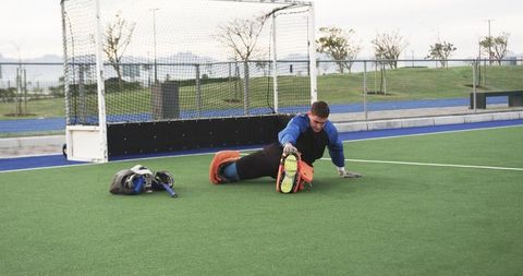 Field hockey goalkeeper stretching on turf field