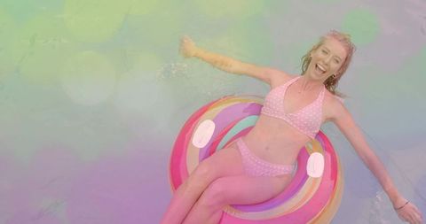 Relaxing on colorful donut float in pastel pool wearing pink polka-dot bikini, smiling