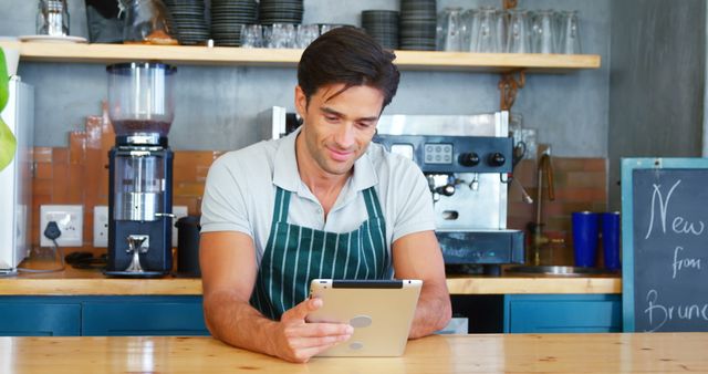 Small business owner standing at coffee shop counter using tablet for work tasks. Perfect for illustrating concepts of small business management, entrepreneurship, modern technology in small businesses, barista lifestyle, and service industry activities.