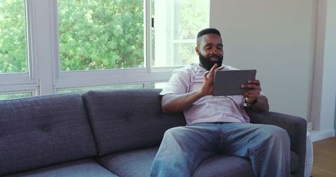 Man relaxing on couch using tablet with earbuds in bright living room