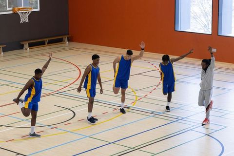 Male Basketball Team Stretching with Coach on Indoor Court