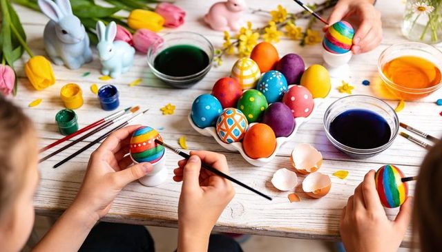 Children decorating colorful easter eggs with paints and brushes on rustic wooden table