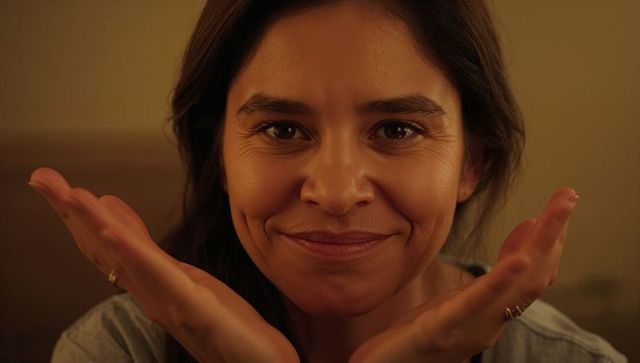 Warm closeup portrait of smiling woman cradling face with hands, cozy amber lighting