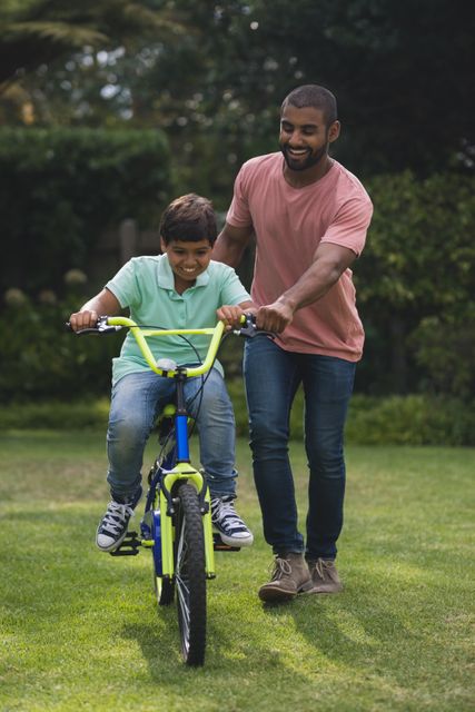 Father assisting son while riding bicycle at park