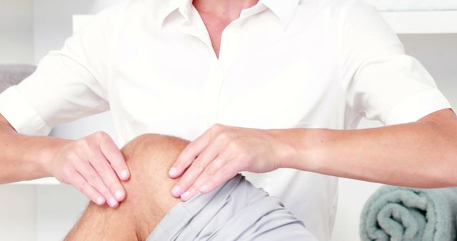 Physiotherapist applying massage techniques to a patient's knee for rehabilitation therapy. Ideal for use in materials related to physical therapy, injury recovery, healthcare services, and professional medical treatments. Useful for illustrating pain relief treatments, physiotherapy sessions, and professional healthcare guidance.