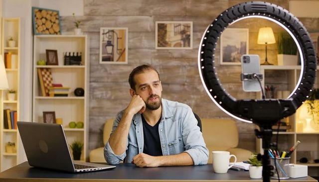 Man Recording Live Stream from Home Desk with Ring Light, Laptop, Coffee and Notebook