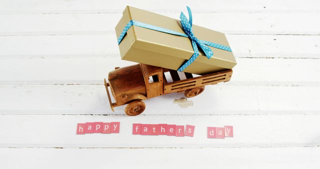 A wooden toy truck carries a gift box tied with a blue ribbon, celebrating Father's Day, with copy space. The festive setup conveys appreciation and love for dads on their special day.
