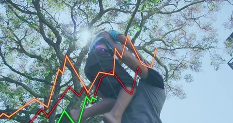 Father lifting son toward sunlit tree canopy active playing outdoors joyful family bonding