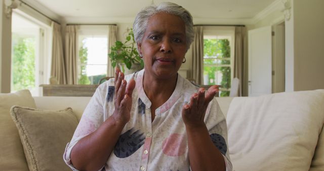 Elderly woman clapping hands while speaking in a bright living room. Ideal for use in healthcare, senior lifestyle, and community engagement materials.