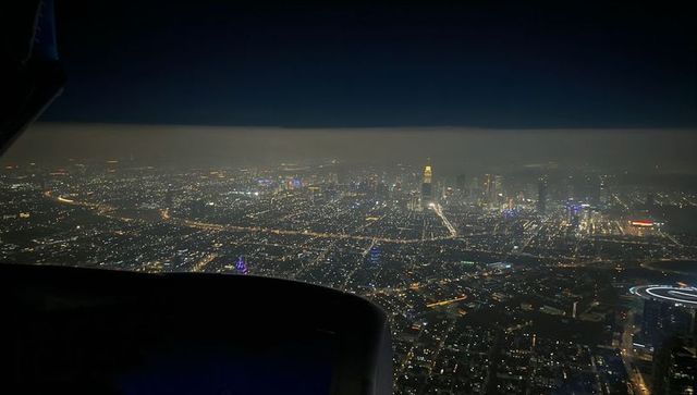 Cruising over city lights at night from airplane window, sprawling illuminated metropolis below