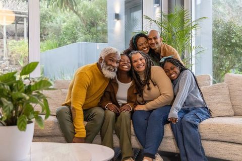 Multigenerational african american family embracing on couch in bright modern living room with house