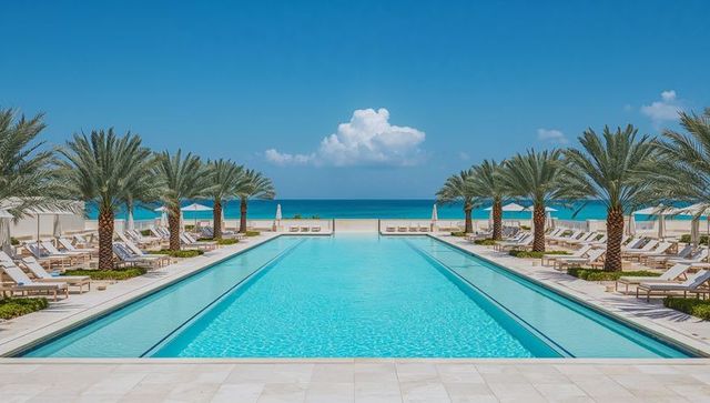 Resort infinity pool stretching toward turquoise ocean with palm-lined loungers, clear sky