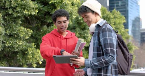Multicultural college students collaborating on tablet outdoors on urban campus path
