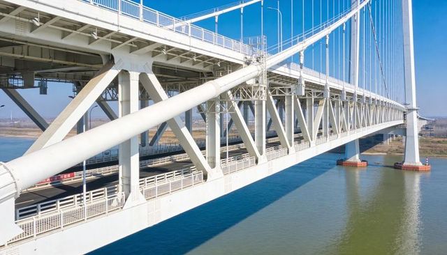 White Suspension Bridge Spanning Wide River with Steel Truss and Cables, Drone View