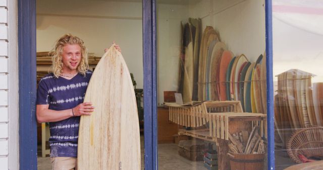 Young Surfer Holding Wooden Surfboard Outside Shop with Multiple Surfboards - Download Free Stock Images Pikwizard.com