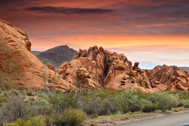 The image captures the stunning sunset over Red Rock Canyon with dramatic clouds and rugged rocks in the foreground, providing an awe-inspiring vista. Ideal for use in travel brochures, outdoor adventure marketing materials, nature photo collections, and inspirational posters emphasizing natural beauty and exploration.