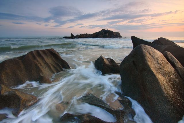Dynamic image showing waves crashing against rocks along the coastline at sunrise. Perfect for use in travel brochures, nature magazines, website headers, or backgrounds related to coastal environments, marine life, or tranquility in nature.