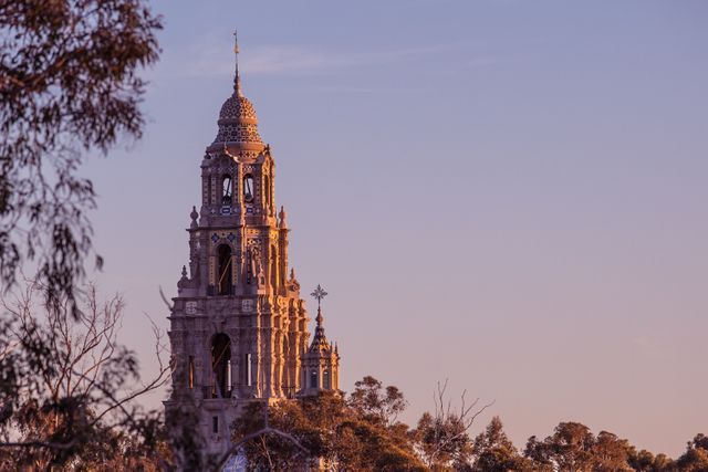 Historic tower stands tall, illuminated by the golden hues of the setting sun, surrounded by trees creating a serene landscape. Ideal for use in travel blogs, historical architecture articles, and scenic landscape posters showcasing beautiful landmarks.