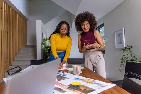 Two women collaborating on moodboard and design layout in modern wooden studio workspace