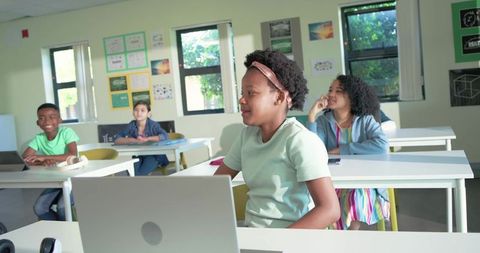 Diverse students collaborating in bright classroom using laptops for digital learning