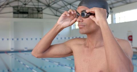 Swimmer Adjusting Goggles Near Indoor Pool Defocused in Background