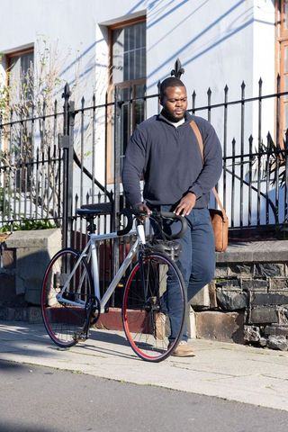 African american man walking with road bicycle and leather bag on sunny urban sidewalk