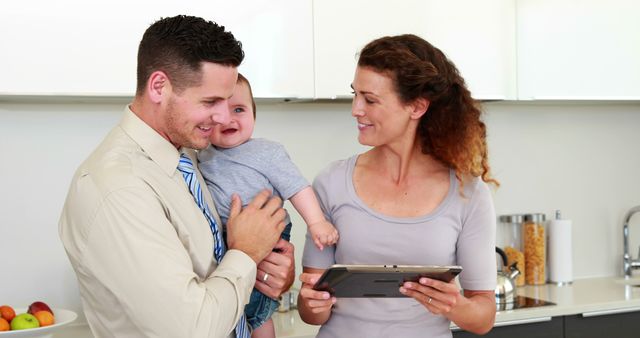 Parents using tablet pc while father holds baby at home in the kitchen