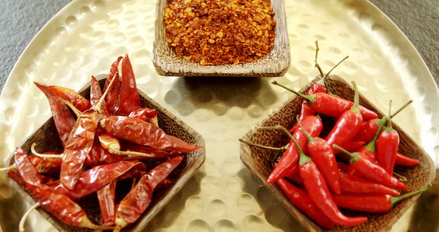 Image showing a variety of red chillies and red chili powder in bowls, placed on a hammered metal tray. The vibrant red color signifies spice and heat, perfect for culinary advertising, cooking blogs, and spice shop promotions. Great for usage in food-related publications, recipes or ingredient lists.