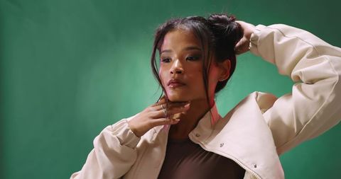 Contemplative fashion model posing with hand on chin fixing hair wearing beige jacket