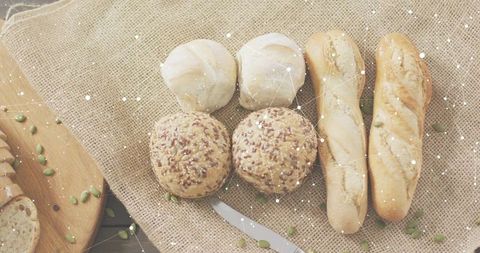 Rustic artisanal bread assortment on burlap with rolls, baguettes, seeds and knife