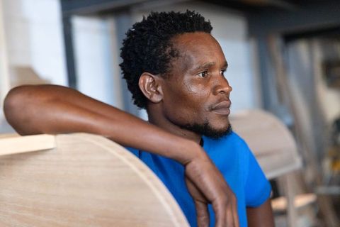 African american craftsman leaning on chair back in woodshop, examining unfinished chairs