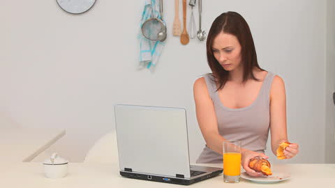 Focused Woman Having Breakfast While Working on Laptop