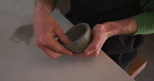 This scene features someone shaping a pottery bowl in a workshop using hands-on techniques. Ideal for content about artistic processes, handmade crafts, and artisan skills. Perfect for illustrating blog posts, articles, or marketing materials related to pottery classes, creative hobbies, or the value of handcrafted items.