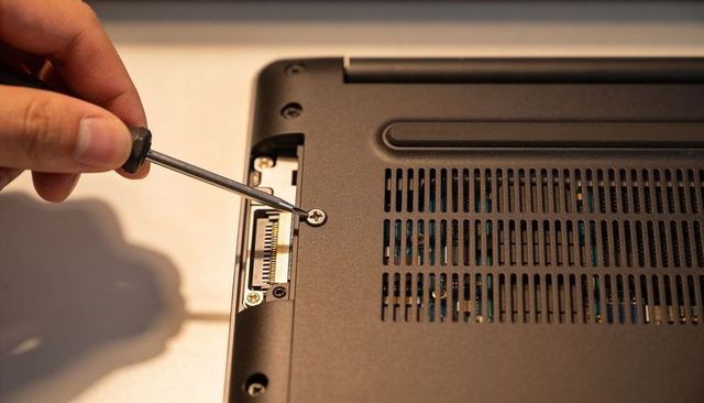 Unscrewing laptop base phillips screwdriver revealing dock port for electronics repair