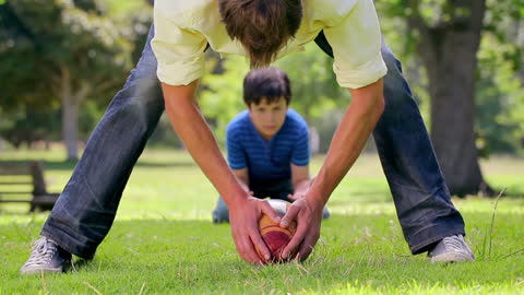 Father Teaching Young Son Basics of Rugby on Grassy Field