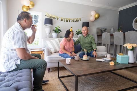 Asian multigenerational family celebrating birthday at home with cake, gifts and balloons