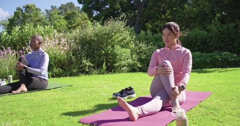 Outdoor yoga partners stretching on sunny lawn with asian woman in pink activewear