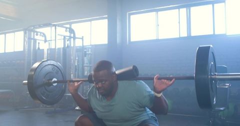 African man performing heavy barbell back squat in gym with foam pad for neck comfort