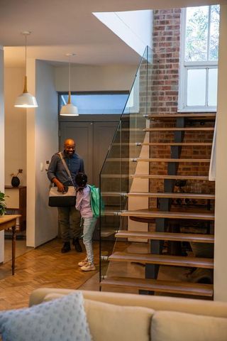 African american father greeting daughter in contemporary entryway with floating stairs