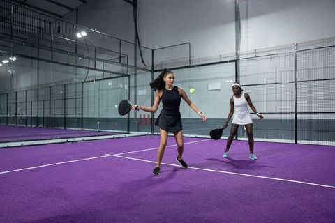 Diverse female teammates playing padel on vibrant purple court with glass walls