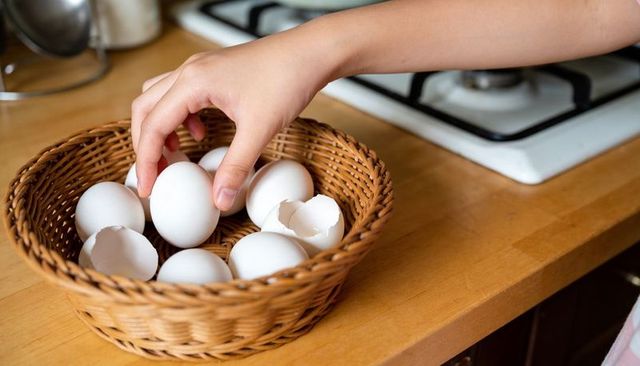 Child hand reaching for white eggs in woven basket on wooden countertop next to stove