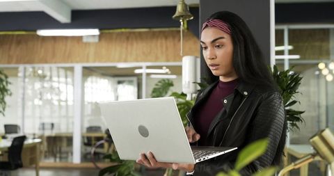 Focused young woman using laptop in modern coworking space with indoor plants