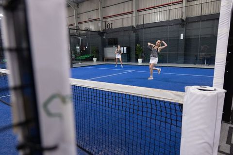 Female teammates playing padel on blue indoor court celebrating point and laughing